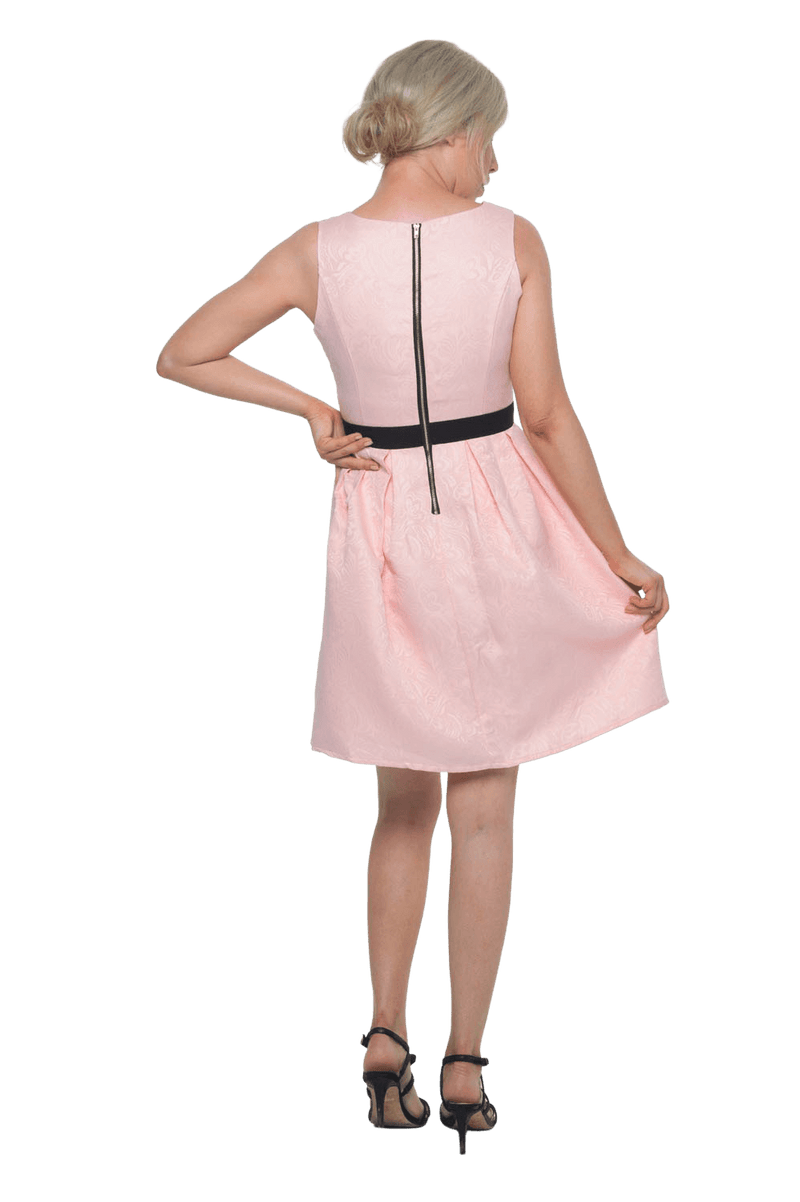 Petite model facing the back wearing pink cocktail dress, featuring a boat neckline, back zip and a feature black sash across the waist. Marie available in sizes 6-18