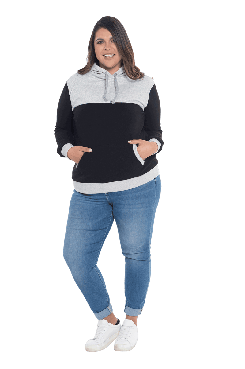 Curvy model facing camera wearing black hoodie with grey panel over chest, shoulders, and top of back, featuring front pocket, and grey highlights at pocket openings and sleeve cuffs. Olivia hoodie available in sizes 6-26