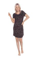 Petite model facing camera wearing black with small red rose patterned mid thigh length nightie, featuring rounded neckline, scooped hemline with short sleeves. Penny available in sizes 6-18