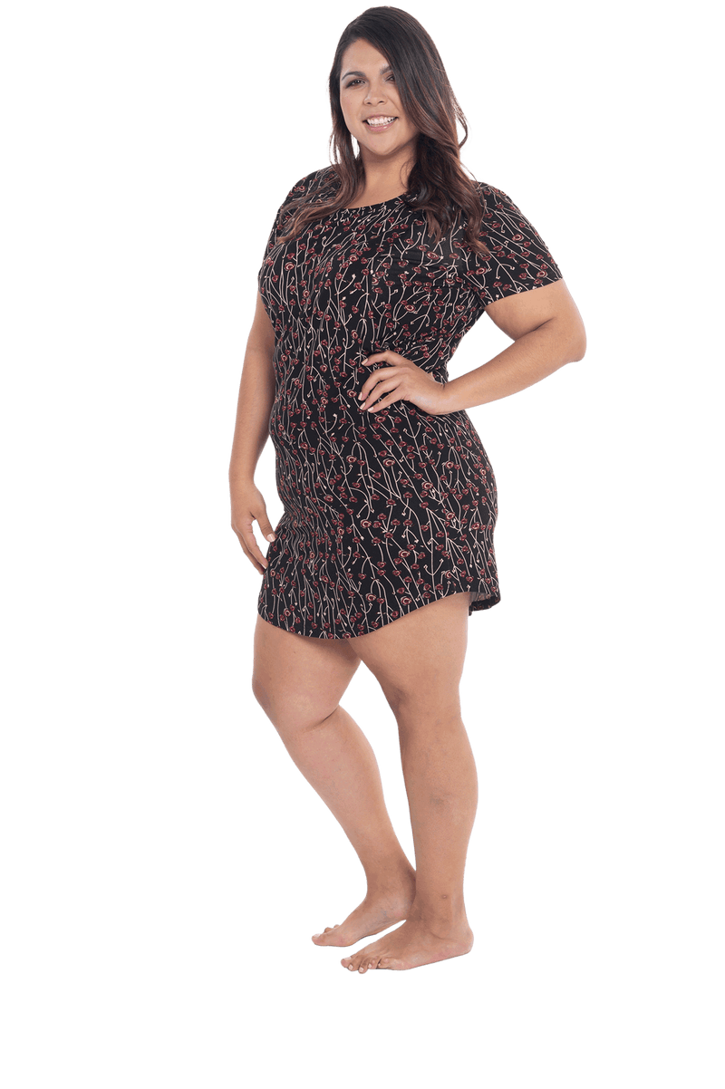 Curvy model facing the side wearing black with small red rose patterned mid thigh length nightie, featuring rounded neckline, scooped hemline with short sleeves. Penny available in sizes 6-18