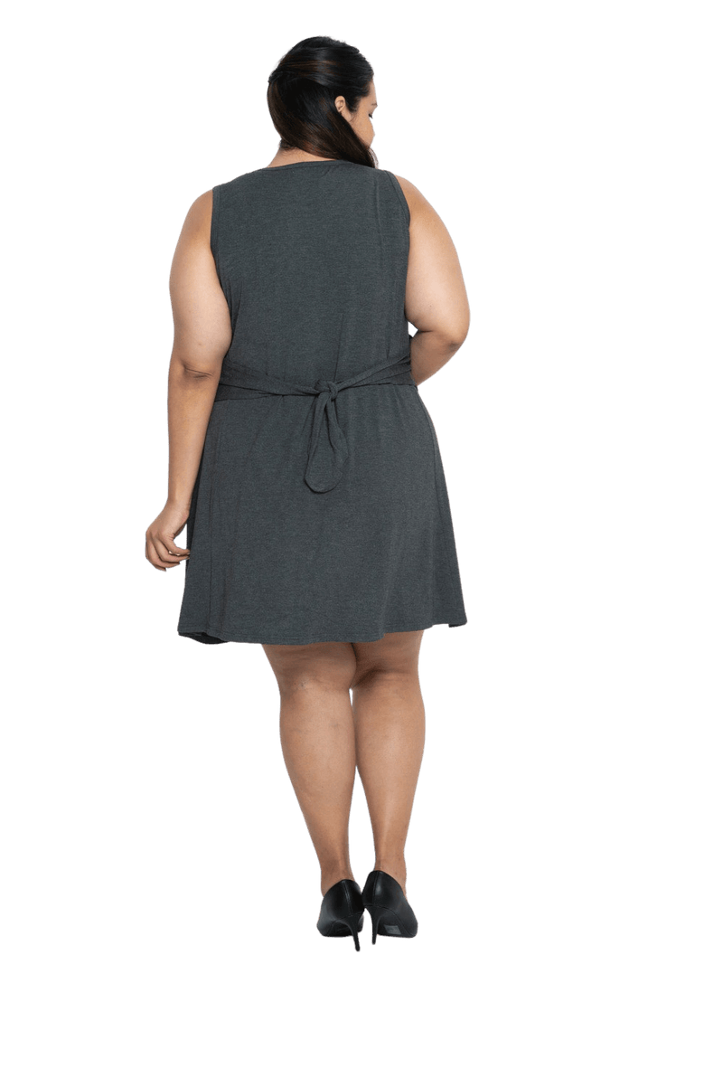 Curvy model facing the back wearing charcoal grey mid thigh length dress, featuring rounded neckline, pockets and a waist sash tied at the back. Peyton available in sizes 6-26