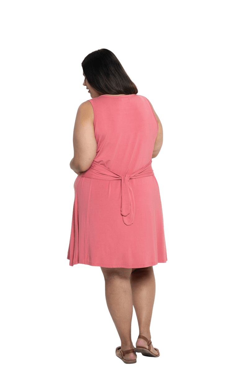 Curvy model facing the back wearing dusty pink mid thigh length dress, featuring rounded neckline, pockets and a waist sash tied at the back. Peyton available in sizes 6-26