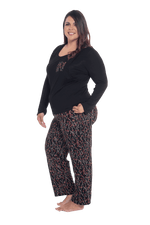 Curvy model facing the side wearing long sleeved pyjamas with pants. Top is black with contrast breast pocket matching pants. Pants are black with small red rose pattern, featuring pockets, and elasticated waist with pull tie. Piper available in sizes 6-26