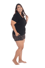 Curvy model facing the side wearing short sleeved pyjamas with shorts. Top is black with contrast breast pocket matching shorts. Shorts are black with small red rose pattern, featuring pockets, and elasticated waist with pull tie. Poppy available in sizes 6-26