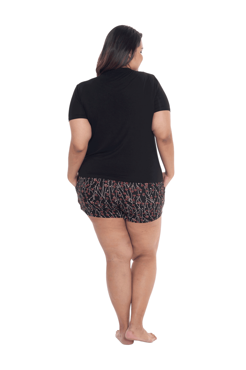 Curvy model facing the back wearing short sleeved pyjamas with shorts. Top is black with contrast breast pocket matching shorts. Shorts are black with small red rose pattern, featuring pockets, and elasticated waist with pull tie. Poppy available in sizes 6-26