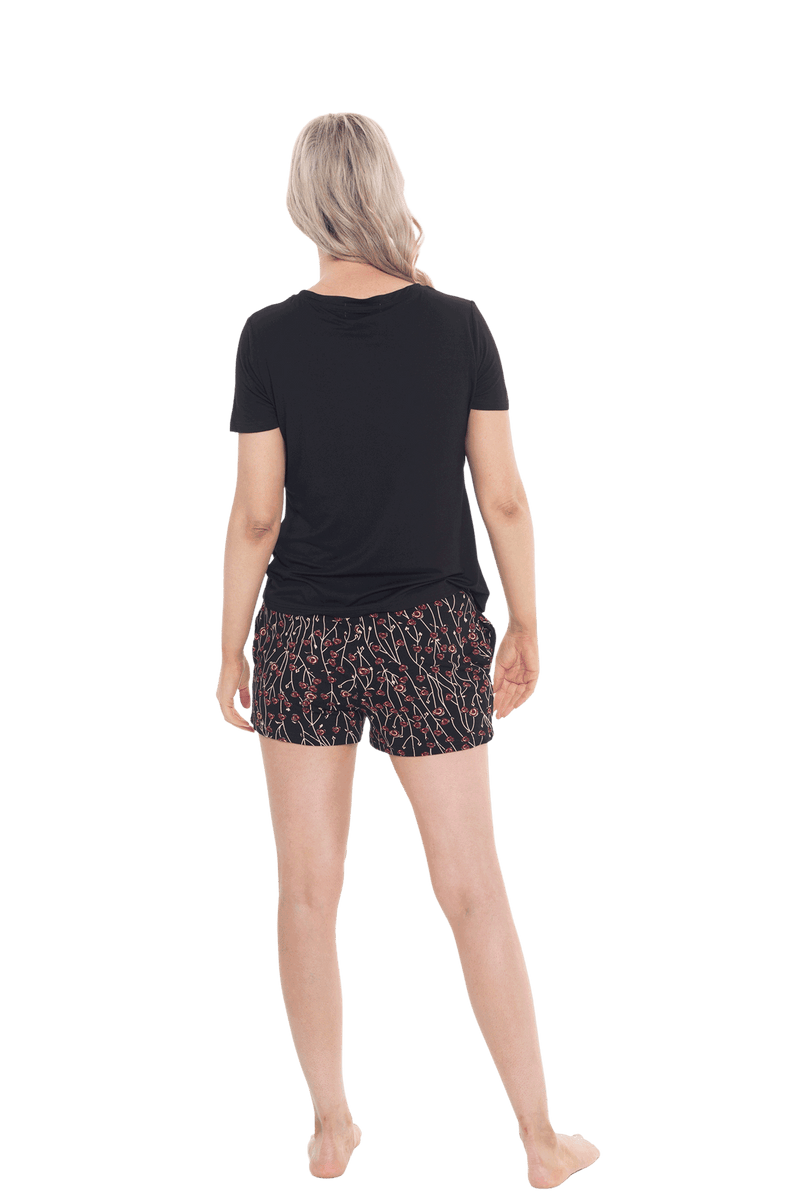 Petite model facing the back wearing short sleeved pyjamas with shorts. Top is black with contrast breast pocket matching shorts. Shorts are black with small red rose pattern, featuring pockets, and elasticated waist with pull tie. Poppy available in sizes 6-26