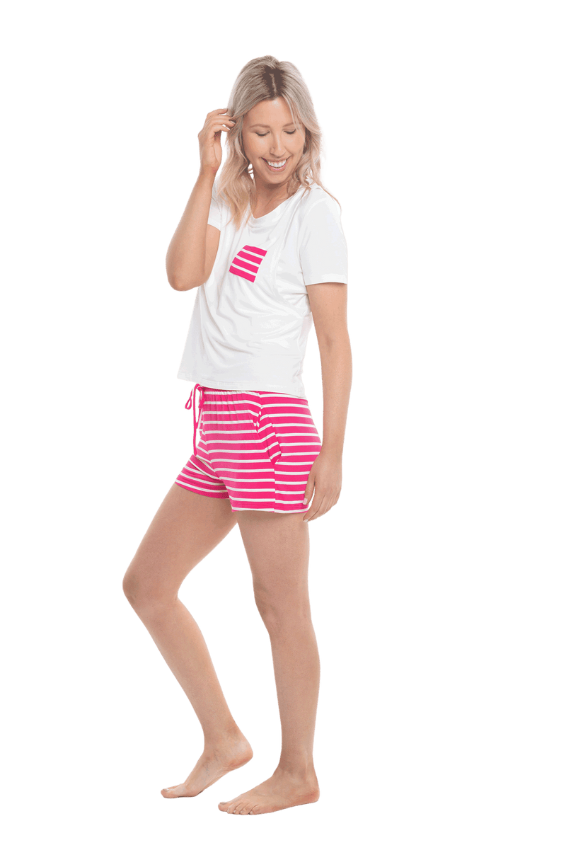 Petite model facing the side wearing short sleeved pyjamas with shorts. Top is white with contrast breast pocket matching shorts. Shorts are hot pink and white stripe, featuring pockets, and elasticated waist with pull tie. Poppy available in sizes 6-18
