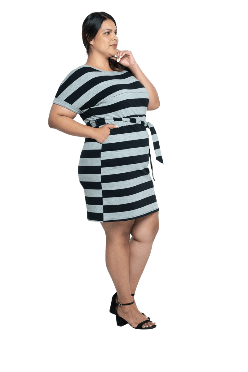 Curvy model facing the side wearing charcoal grey and black striped t-shirt dress, featuring rounded neckline, pockets, belt feature, and capped sleeves. Quinn available in sizes 6-26