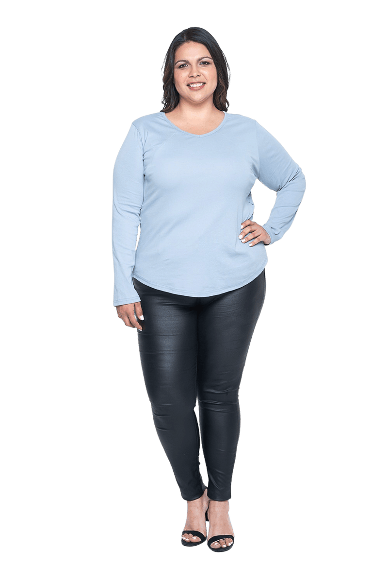 Curvy model facing camera wearing dusty blue long sleeved top, featuring soft V-neck and a scooped hem. Reese available in sizes 6-26