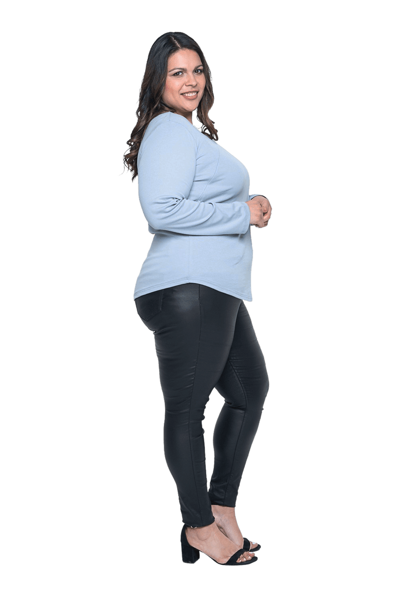 Curvy model facing the side wearing dusty blue long sleeved top, featuring soft V-neck and a scooped hem. Reese available in sizes 6-26