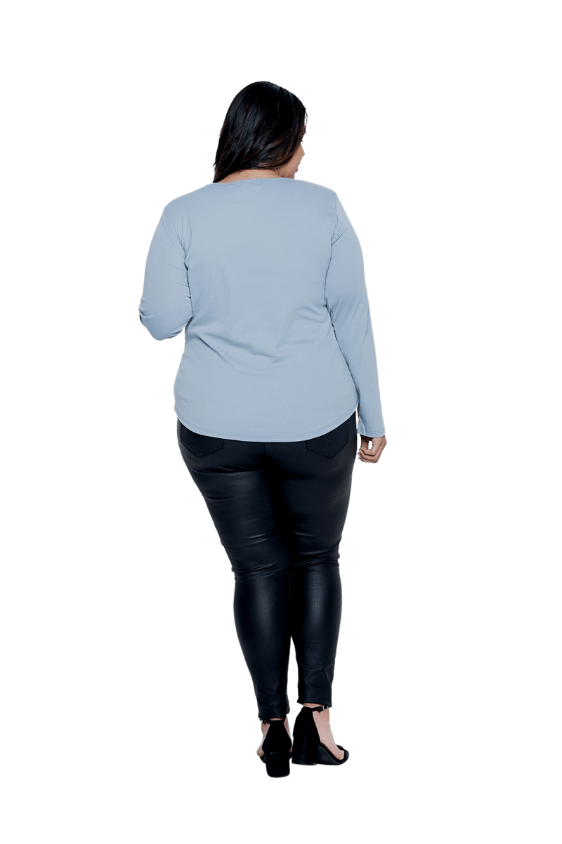 Curvy model facing the back wearing dusty blue long sleeved top, featuring soft V-neck and a scooped hem. Reese available in sizes 6-26