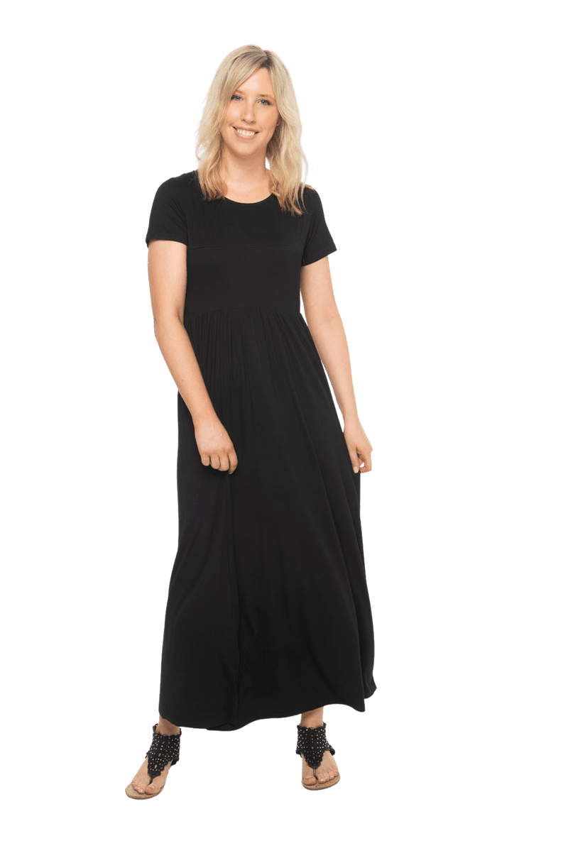 Petite model facing the camera wearing black maxi dress, featuring  rounded neckline, and a gently fitted bodice, gathering above the waist. Riley available in sizes 6-26