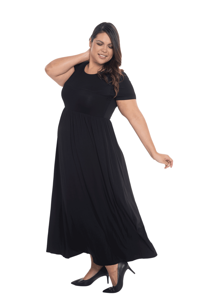 Curvy model facing the side wearing black maxi dress, featuring  rounded neckline, and a gently fitted bodice, gathering above the waist. Riley available in sizes 6-26