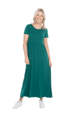 Petite model facing the camera wearing bottle green maxi dress, featuring  rounded neckline, and a gently fitted bodice, gathering above the waist. Riley available in sizes 6-26