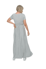 Petite model facing the back wearing light grey and white striped maxi dress, featuring rounded neckline, and a gently fitted bodice, gathering above the waist. Riley available in sizes 6-18