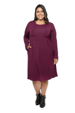 Curvy model facing camera wearing long sleeved, knee length burgundy dress. Featuring pockets, a rounded neckline, and pleated front. Robyn available in sizes 6-26