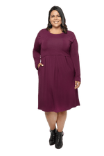 Curvy model facing camera wearing long sleeved, knee length burgundy dress. Featuring pockets, a rounded neckline, and pleated front. Robyn available in sizes 6-26