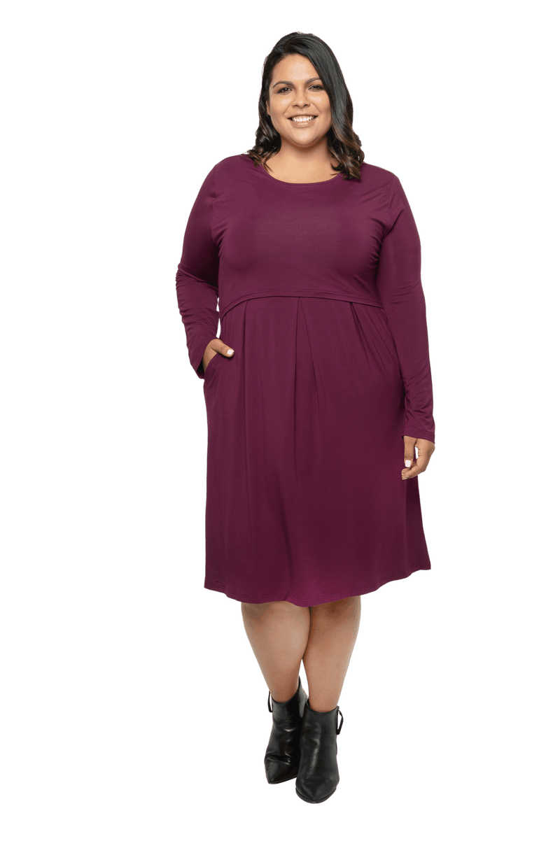 Curvy model facing camera wearing long sleeved, knee length burgundy dress. Featuring pockets, a rounded neckline, and pleated front. Robyn available in sizes 6-26