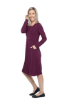 Petite model facing the side wearing long sleeved, knee length burgundy dress. Featuring pockets, a rounded neckline, and pleated front. Robyn available in sizes 6-26