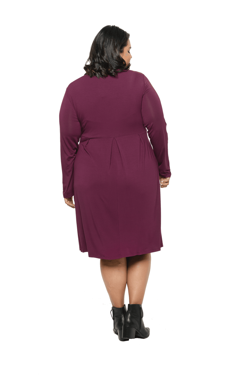 Curvy model facing the back wearing long sleeved, knee length burgundy dress. Featuring pockets, a rounded neckline, and pleated front. Robyn available in sizes 6-26