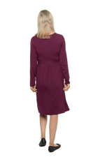 Petite model facing the back wearing long sleeved, knee length burgundy dress. Featuring pockets, a rounded neckline, and pleated front. Robyn available in sizes 6-26