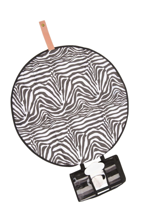 The All Rounder Change Mat shown laying flat. A round mat in Zebra print with a mesh pocket attached for storing wipes and nappies. The sand coloured closing strap is shown at the top of the mat.