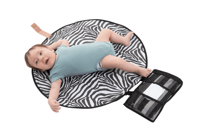 The All Rounder Change Mat shown laying flat with a baby lying on top. Baby has brown hair and wears blue short sleeves onesie. His tiny little toes and fingers are so cute!