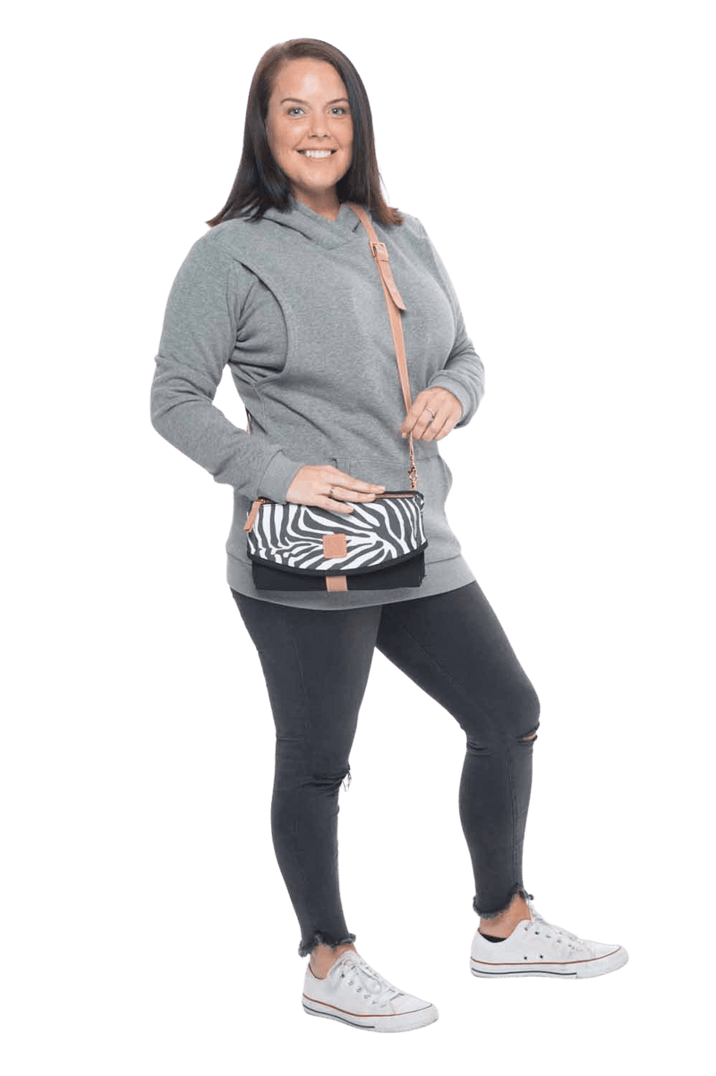 Model wears The All Rounder Change Mat in zebra print using the shoulder strap across her body. Model is brunette and wears a grey Andrea hoodie, black jeans and white shoes.