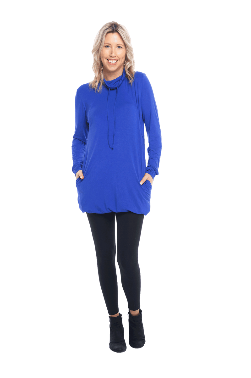 Petite model facing the camera wearing cobalt blue long sleeved tunic as a top with black pants, featuring pockets and a faux hoodie collar in a comfy, relaxed fit. Tori available in sizes 6-18