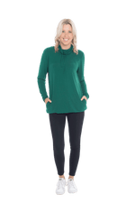 Petite model facing the camera wearing bottle green long sleeved tunic as a top with black pants, featuring pockets and a faux hoodie collar in a comfy, relaxed fit. Tori available in sizes 6-26