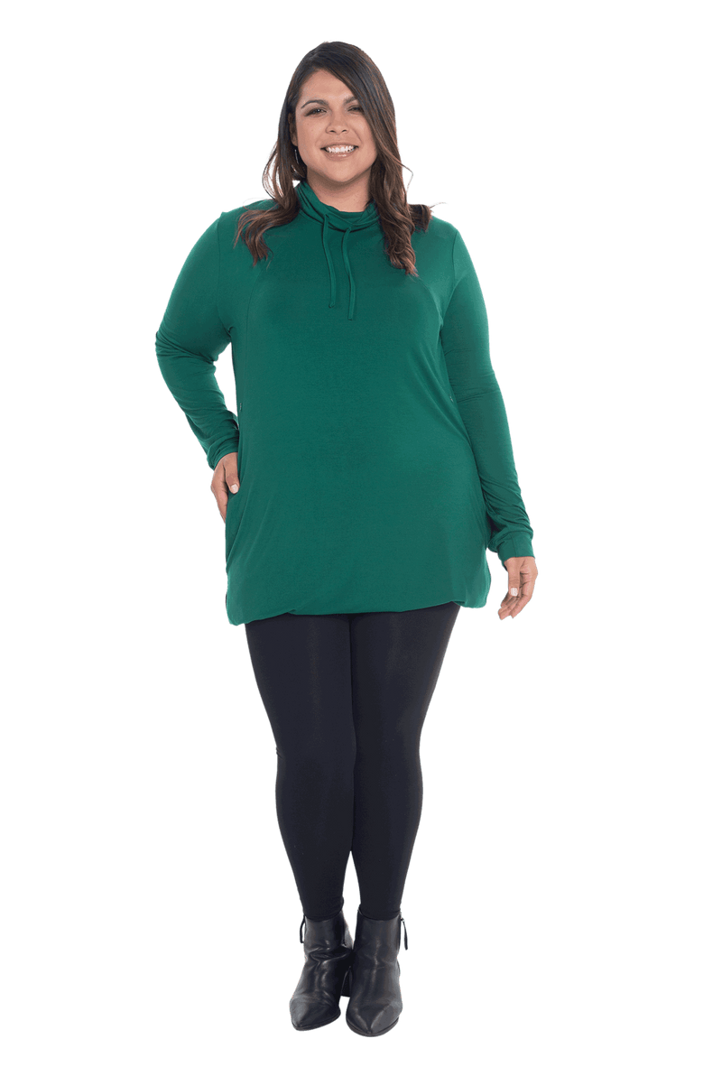 Curvy model facing the camera wearing bottle green long sleeved tunic as a top with black pants, featuring pockets and a faux hoodie collar in a comfy, relaxed fit. Tori available in sizes 6-26